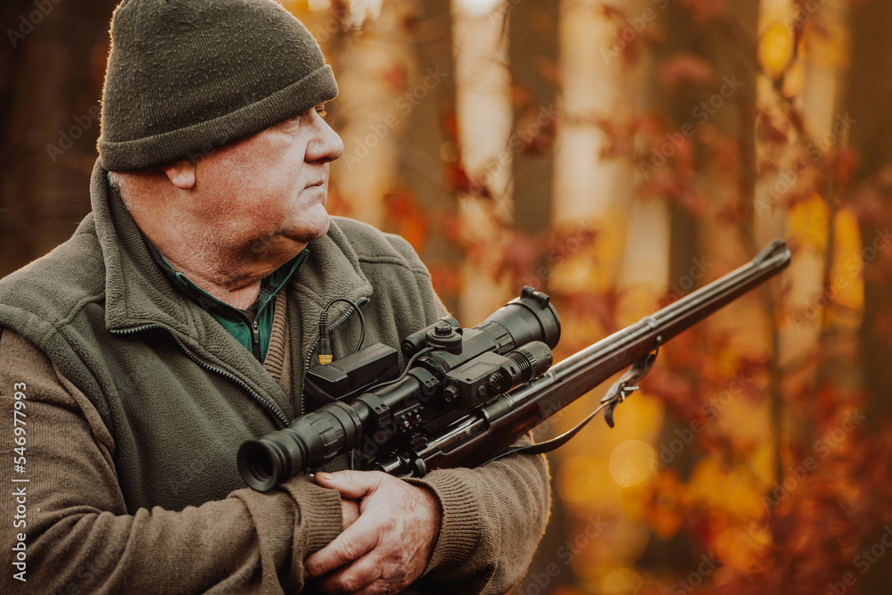 Fototapeta premium Portrait of hunter or ranger with gun or rifle in the forest looking out or hunting of some venison, hunting period, autumn season, hunting and people concept