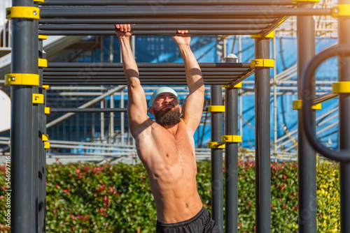 Muscular man in a bandana hanging on the stairs intercepted on the rungs with his hands in the park outdoors. photo