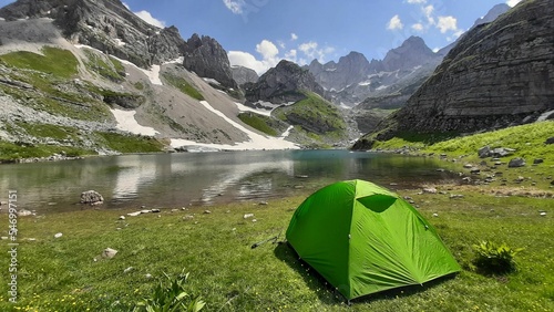 Green tent set near a waterscape surrounded by scenic mountains photo