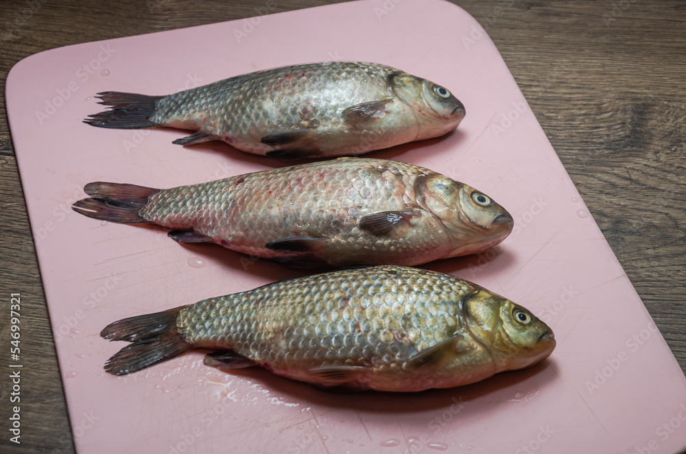 Three raw crucian fish on a cutting board Three raw crucian fish on a cutting board