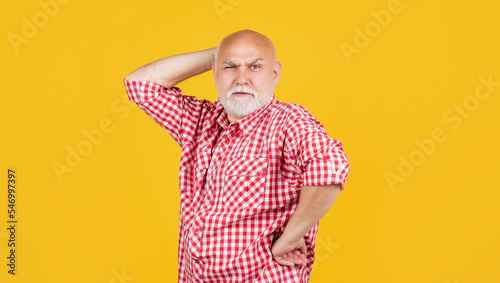 thoughtful senior man in checkered shirt on yellow background