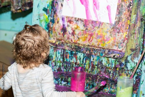 Toddler girl during art project. Kid holds paintbrush. Baby paints with brush on a paper. A girl paints a picture