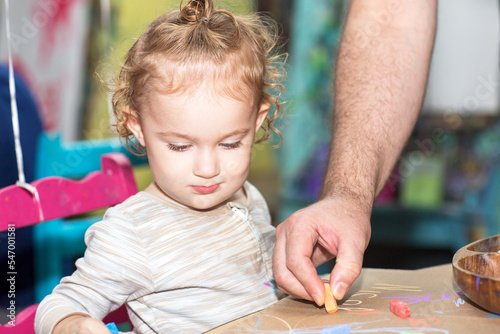Toddler girl during an art project. Kid holds a crayon. Baby works with glue.