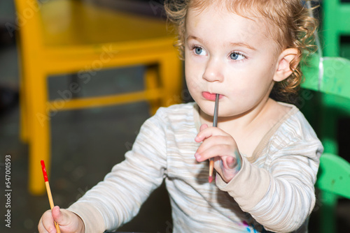 Toddler girl during art project. Kid holds paintbrush. Baby paints with brush on a paper. A girl paints a picture