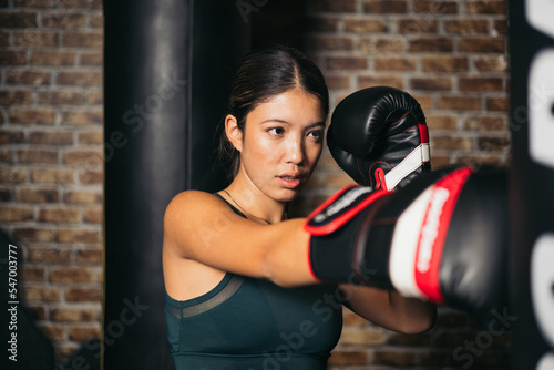 young asian woman kickboxing exercise, training punching bag hard, boxing in gym class. Sports recreational activity, functional training.