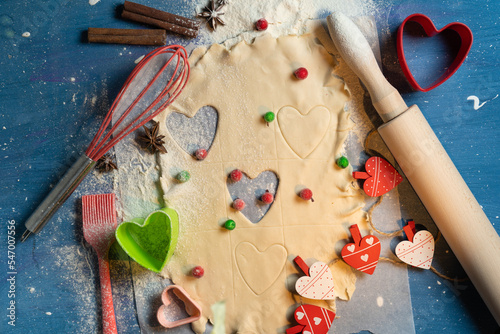 Fairy creative baking. Top view on dough and heart shaped cutters, kitchenware, cinnamon sticks, red, white small heart decorations on blue background. Romantic, love, Valentine day photo