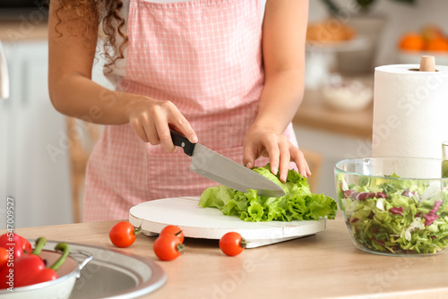 Young woman making fresh salad in kitchen