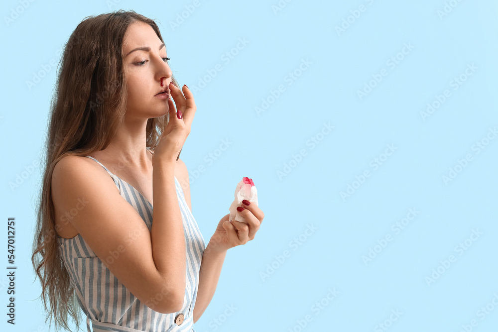 Young woman with nosebleed and tissue on blue background Young woman with nosebleed and tissue on blue background