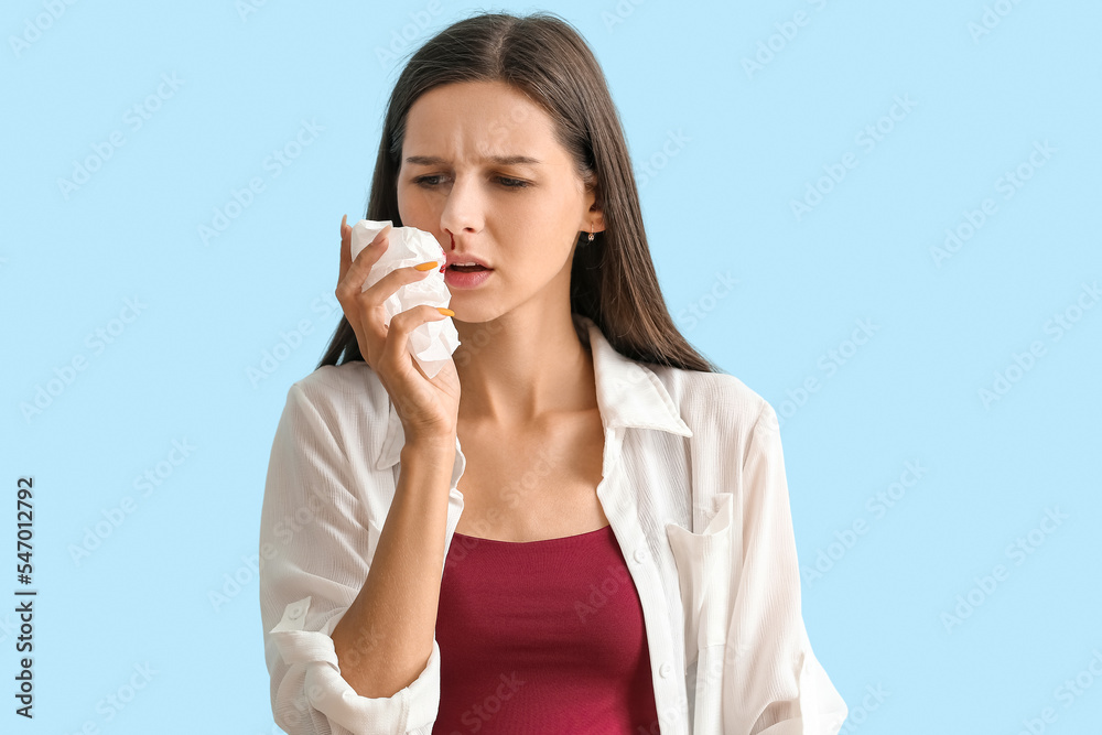 Young woman with nosebleed and tissue on blue background, closeup Young woman with nosebleed and tissue on blue background, closeup
