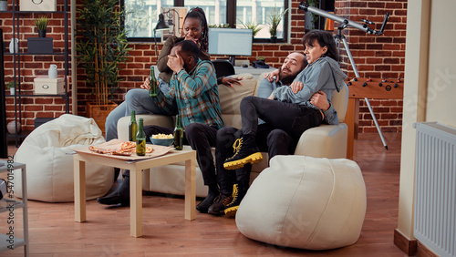 Multiethnic group of friends having terrified reaction while they watch horror movie on tv, being afraid of thriller. Afraid frightened people watching scary film on television channel.