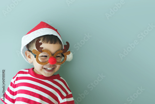 Happy funny Little Asian child boy in Christmas reindeer glasses and Santa hat laughing on blue isolated background. copy space