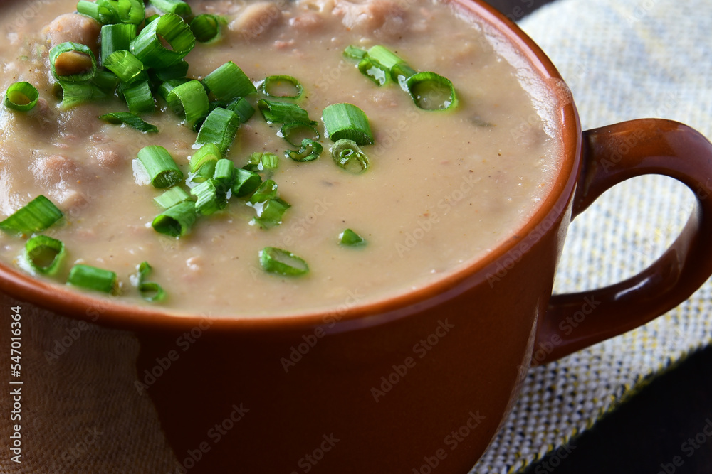 bean broth with chives, bacon and bread, served in an earthenware cup on a wooden base