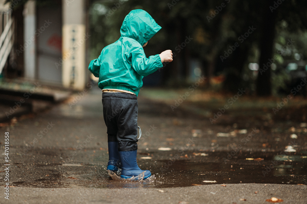 Happy boy playing outside on a rainy day wearing rubber boots and jacket Happy boy playing outside on a rainy day wearing rubber boots and jacket