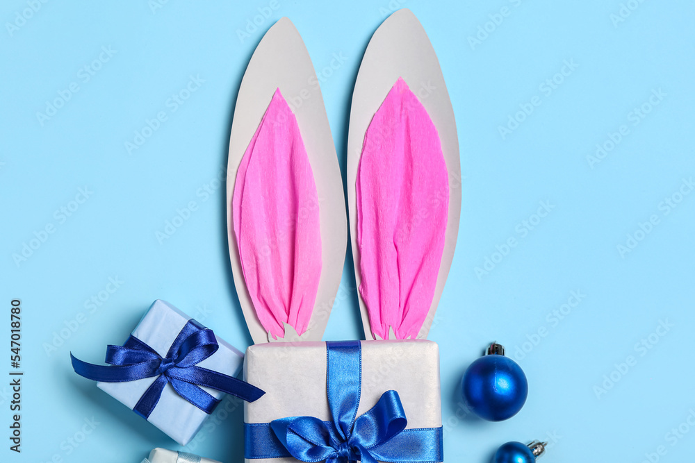 Paper bunny ears with Christmas balls and gifts on blue background