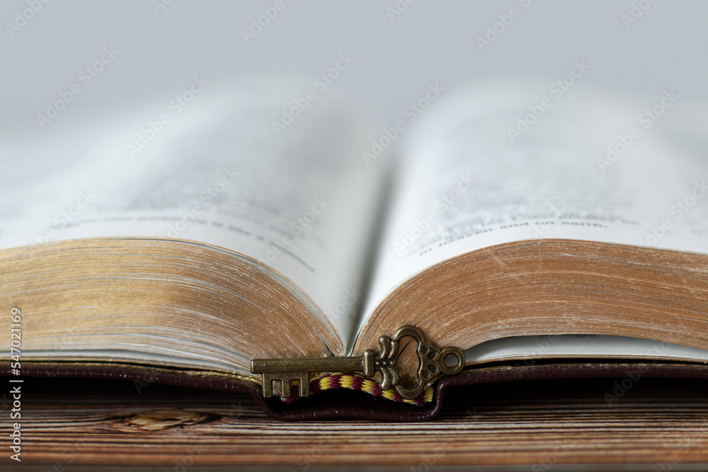 Obraz premium Antique key in front of open Holy Bible Book with golden pages on wooden background. A close-up. Christian biblical concept of revelation, prophecy, unlock mystery from Scripture.