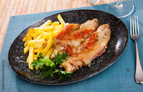 traditional spanish fried pettitoe with fries served on black plate on wooden table. photo