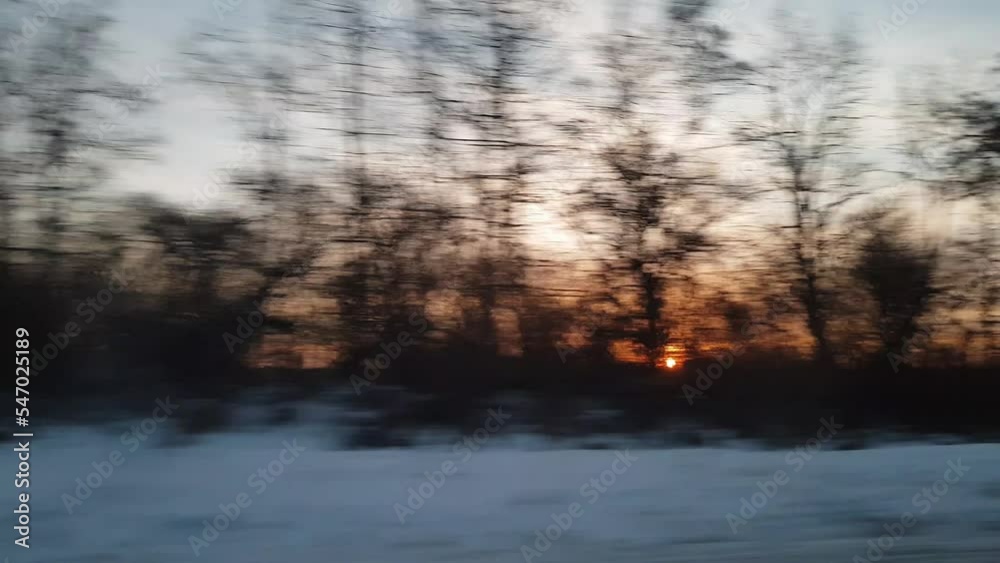 view from window of high-speed train on landscape of beautiful nature wild snowy frosty cold field and bare trees forest sunny evening sunset in winter background. Transport, travel, railway concept