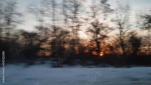 view from window of high-speed train on landscape of beautiful nature wild snowy frosty cold field and bare trees forest sunny evening sunset in winter background. Transport, travel, railway concept
