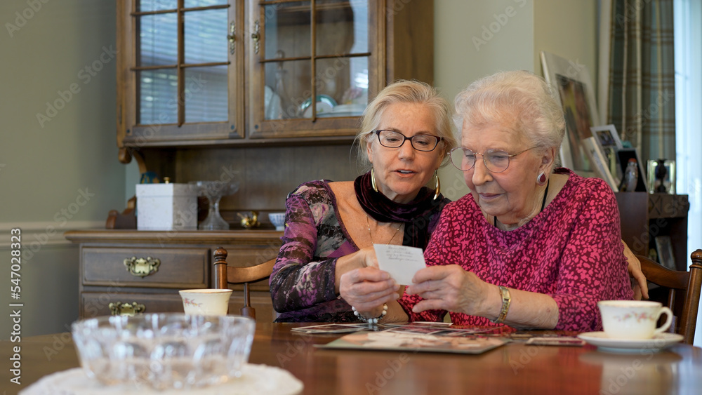 Happy elderly senior woman looks at photos with daughter. Senior woman sitting in the dining room looking at photographs with daughter. Brain training. Memory activity.