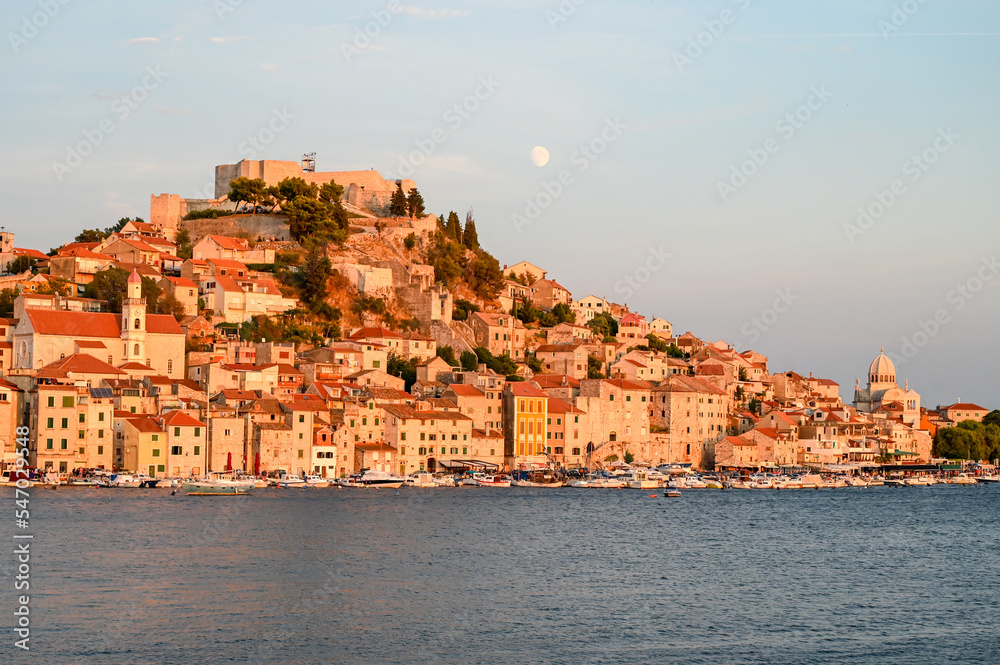 Old town Šibenik, Dalmatia region, Croatia. Buildings, houses, cathedral of St. Jacob and St Michaels fortress on top of hill. Adriatic sea and city of Šibenik at sunset. 