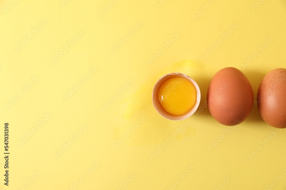 Cracked and whole chicken eggs on yellow background, flat lay. Space for text Cracked and whole chicken eggs on yellow background, flat lay. Space for text