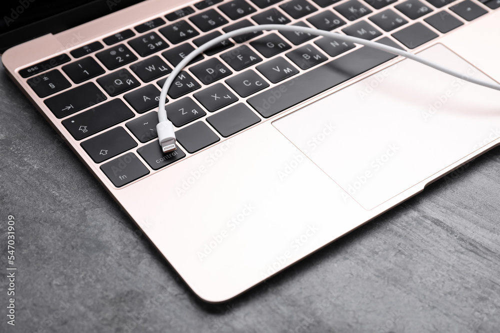 USB cable with lightning connector and laptop on grey table, closeup