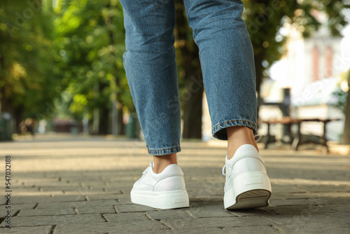 Woman in stylish sneakers walking on city street, closeup