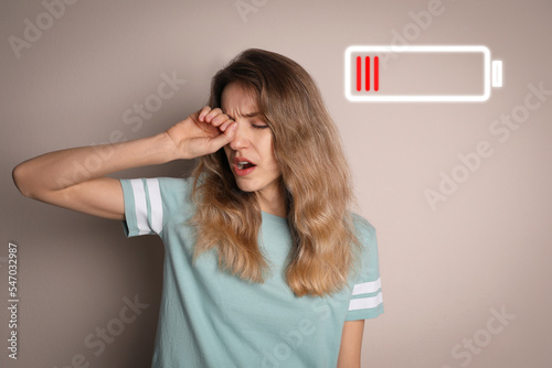 Tired woman yawning and illustration of discharged battery on beige background photo