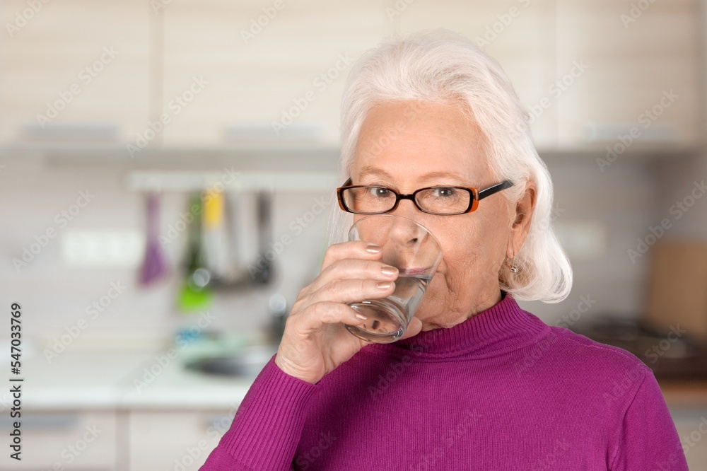 Happy senior woman drinking water at home.