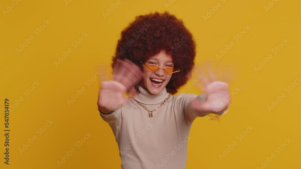 Young funny school girl in glasses smiling friendly at camera and waving hands gesturing hello or goodbye, welcoming with hospitable expression. Teen female child kid isolated on yellow background Young funny school girl in glasses smiling friendly at camera and waving hands gesturing hello or goodbye, welcoming with hospitable expression. Teen female child kid isolated on yellow background
