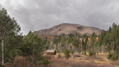 Timelapse of clouds over cabin with fall colors in the mountains, fall foliage in abandoned cabin in the californa sierras, clouds forming before storm, green, orange and red trees during autumn photo