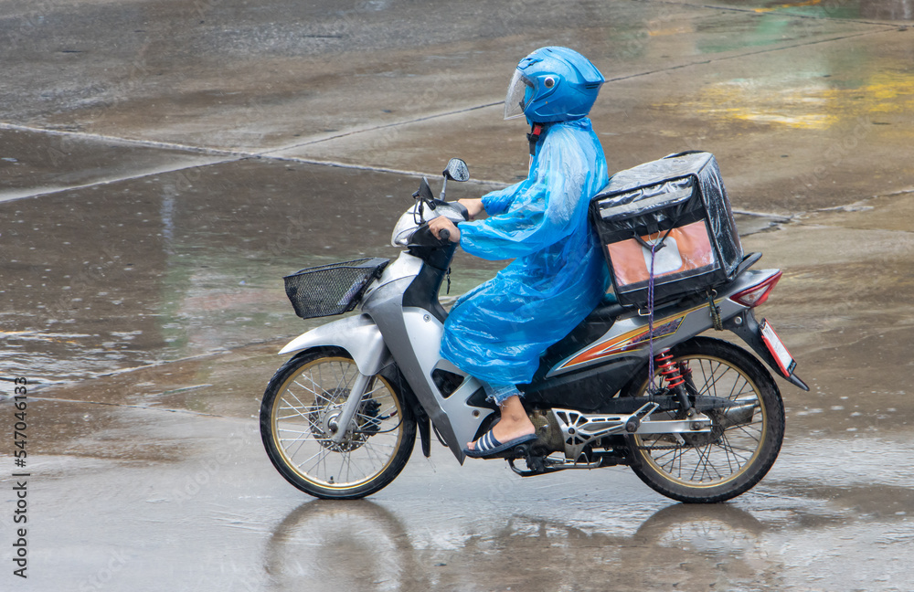 A delivery worker rides a motorcycle with a delivery box at rainy weather A delivery worker rides a motorcycle with a delivery box at rainy weather