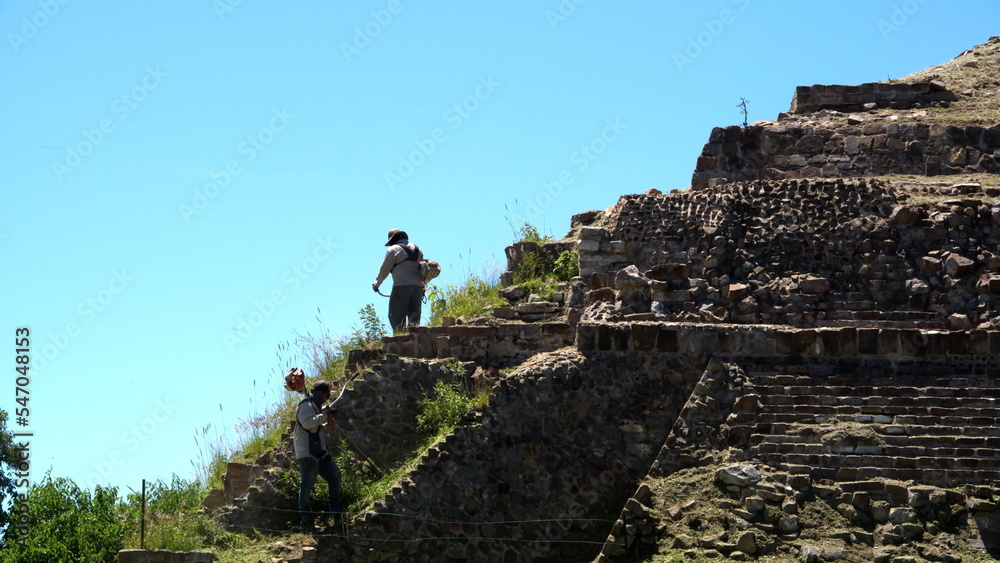 Worker mowing the slope of a pyramid at Monte Alban, in Oaxaca, Mexico Worker mowing the slope of a pyramid at Monte Alban, in Oaxaca, Mexico