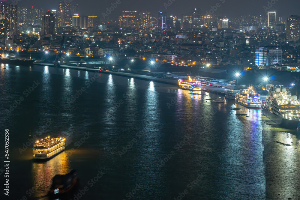 Fototapeta premium Classic night skyline under full lights of Ho Chi Minh City with Saigon river and large tourist boat. Travel and landscape concept.