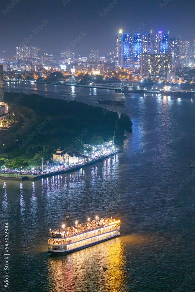 Naklejka premium Classic night skyline under full lights of Ho Chi Minh City with Saigon river and large tourist boat. Travel and landscape concept.