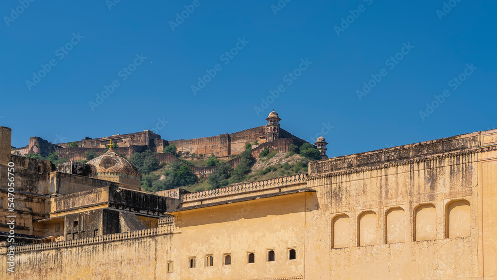 The fortress walls of the ancient Amber Fort are built of orange sandstone. Against the background of the blue sky, on a hill, towers, domes, arched openings are visible. India. Jaipur