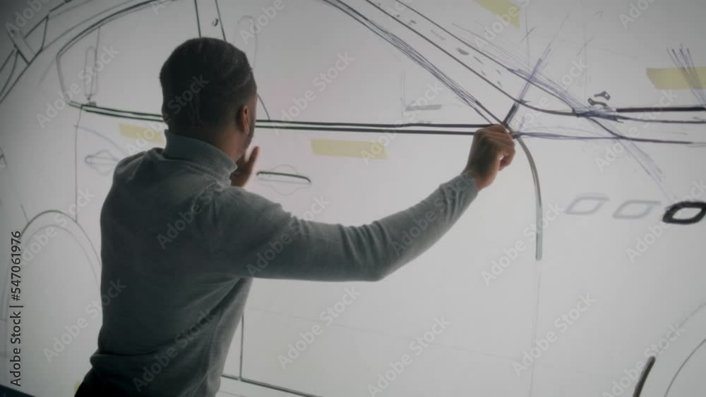 African American automotive male engineer creating sketch with tools on whiteboard, developing new generation electric car design with colleague. Work in modern car design development studio.