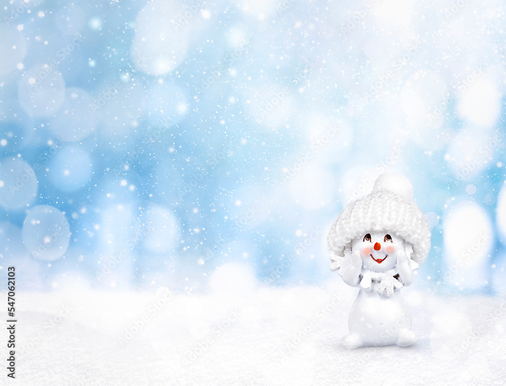 a snowman in a hat stands on the snow on a blue background with bokeh