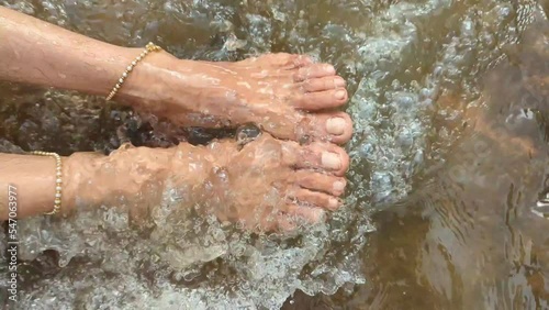 feet of a woman with anklets being washed by flowing water in a river stream 