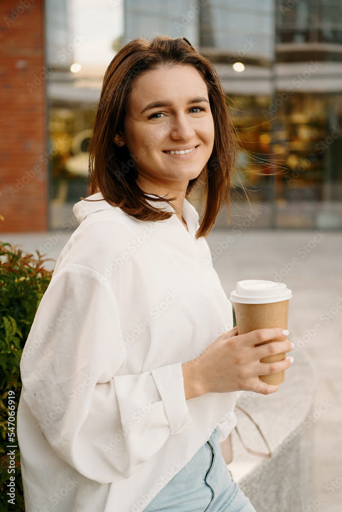 Vertical photo of happy woman in casual sitting oudoor in city and drinking her morning coffee Vertical photo of happy woman in casual sitting oudoor in city and drinking her morning coffee