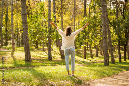 Freedom. Image of young woman with raised arms in middle of forest in sunlight © Vulp