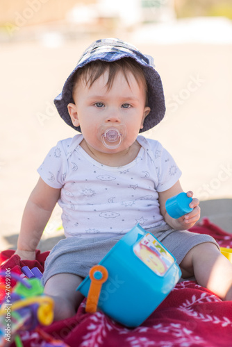 Little baby's face with pacifier. Portrait of a beautiful child, close up on sand background. Boy wears a sunny hat