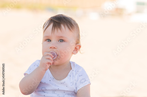 Little baby's face with pacifier. Portrait of a beautiful child, close up on sand background. 