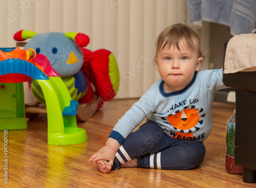 Little smiling baby sits on the floor. Portrait of a beautiful child, close up on sand background. 