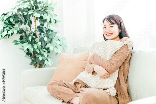家のリビングのソファにクッションを持ちながら座る笑顔の日本人女性 