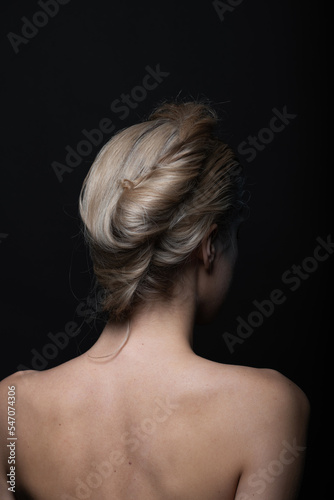 Natural beauty, make-up and fashion concept. Beautiful woman portrait with naked shoulders and hair bun. Model standing back to camera in black studio background with copy space