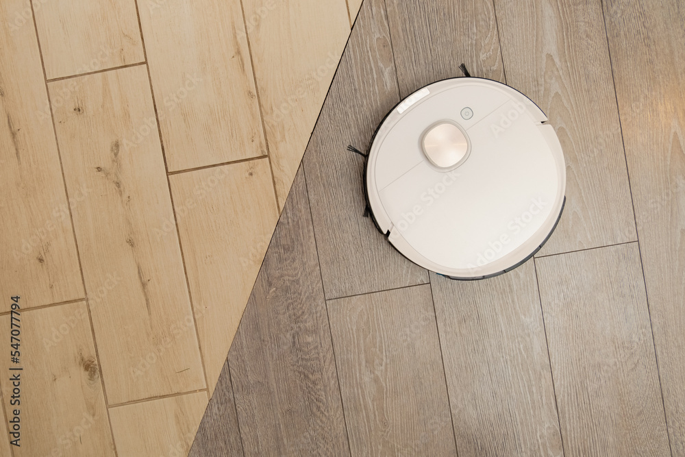 White autonomous robotic vacuum cleaner cleans woodpatterned tiled and