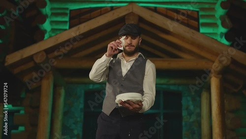 Young man breaking smashing many plates on his hand. Male artist wearing classic vest and hat quickly brakes , smashes glass dishes . Traditional Greek wedding dance kefi . Broken shards falling down 