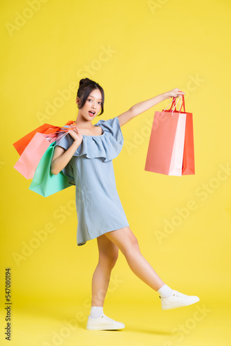 image of a beautiful asian girl in a dress holding a shopping bag in her hand posing on a yellow background