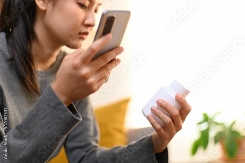 Young Asian girl holding a smartphone and a pill bottle in hands